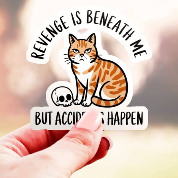 Sticker Of An Orange Tabby Cat Sitting Next To A Skull, With Text That Says Revenge Is Beneath Me, But Accidents Happen.