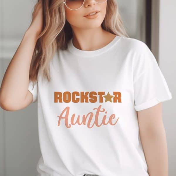 Woman Wearing A White T-Shirt That Says Rockstar Auntie In Orange And Peach Text With A Gold Star.