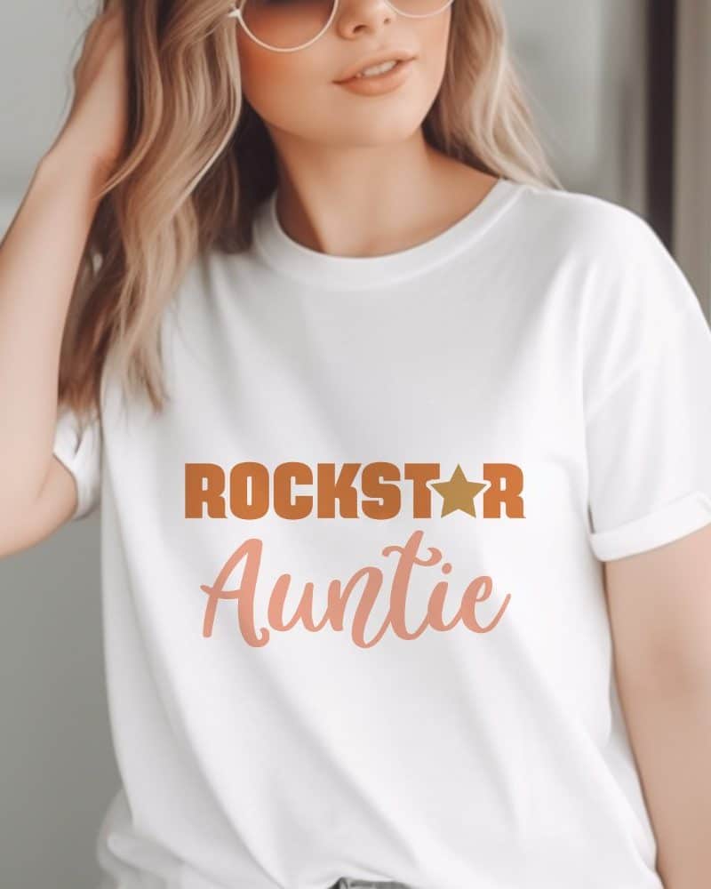 Woman wearing a white t-shirt that says Rockstar Auntie in orange and peach text with a gold star.