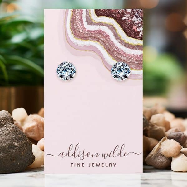 Pair Of Round, Clear Stud Earrings Displayed On A Pink Jewelry Card.