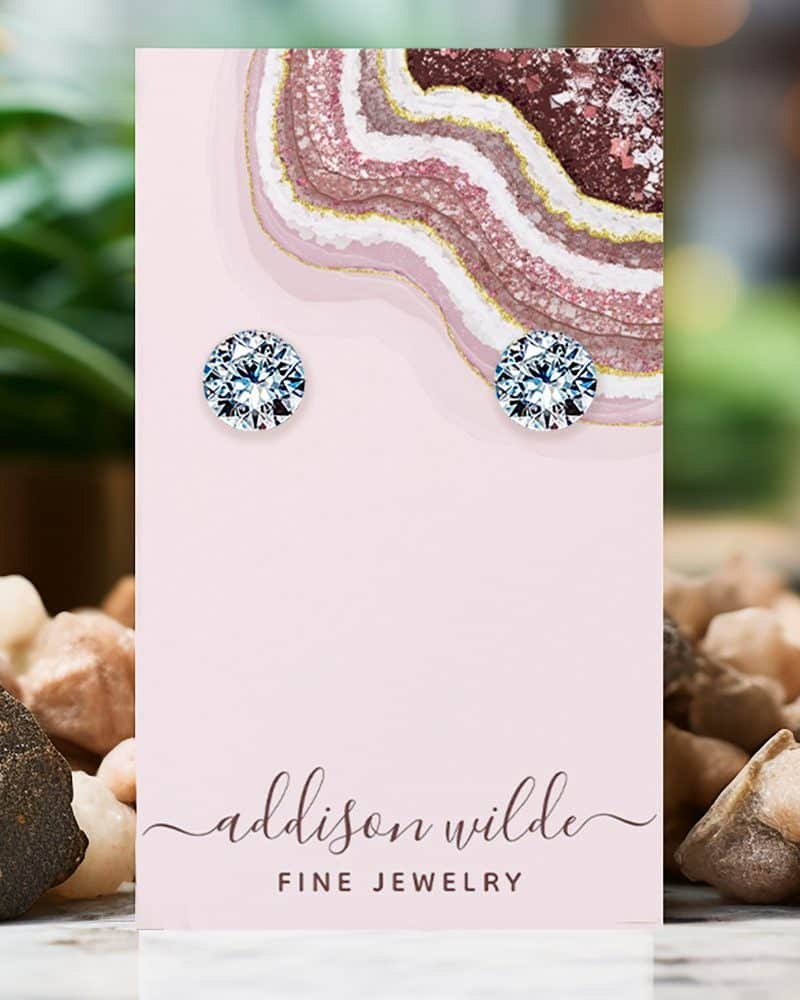 Pair of round, clear stud earrings displayed on a pink jewelry card.