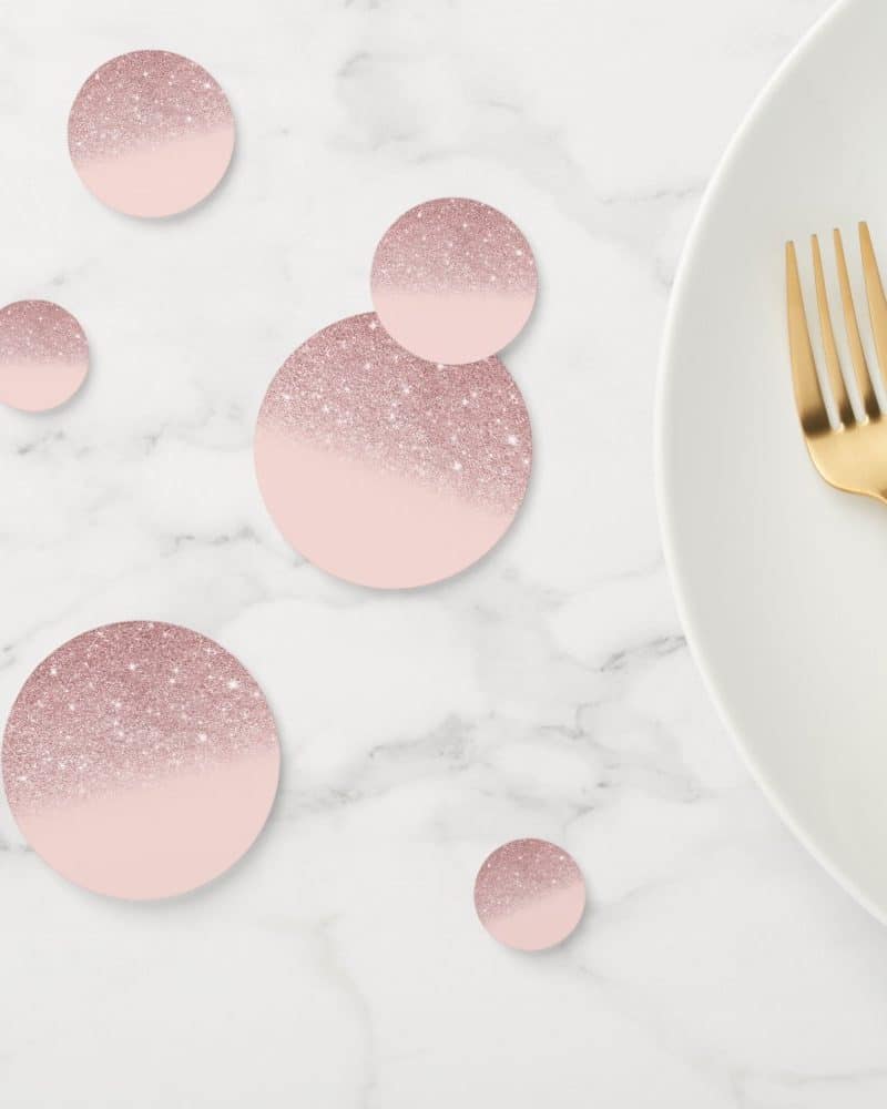 Rose gold glitter confetti circles on a marble surface next to a gold fork and white plate.