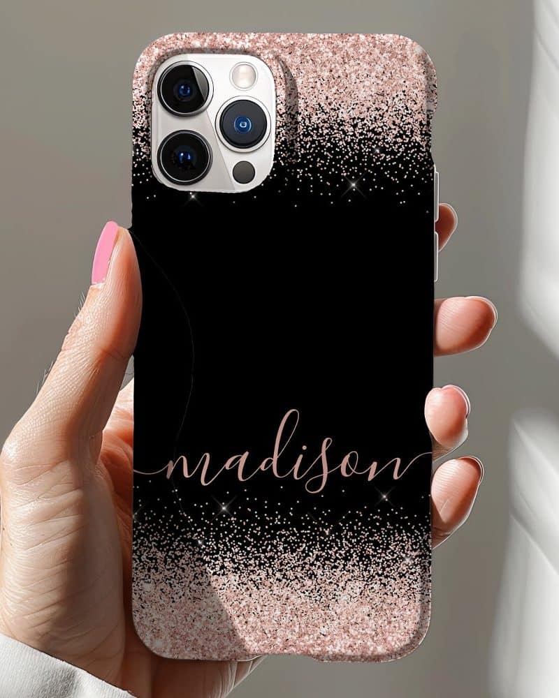 A hand holding a black iPhone case with rose gold glitter at the top and bottom, and the name Madison in rose gold script in the center.