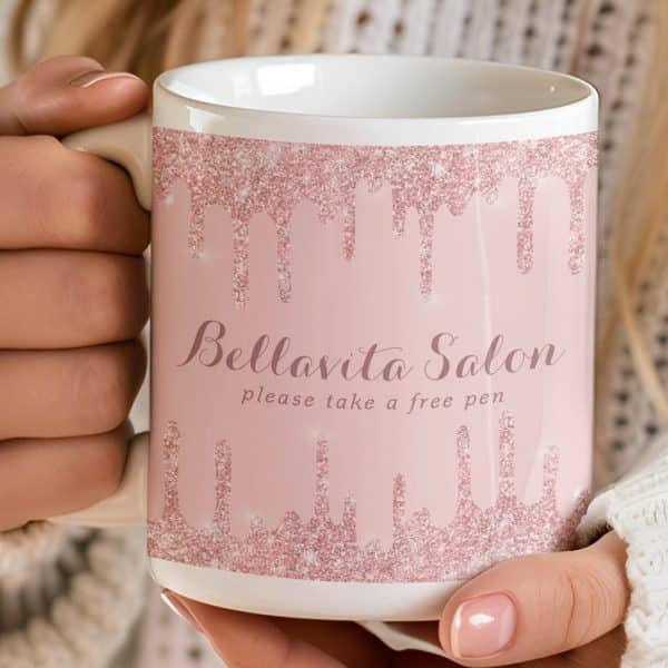 A Person Holding A Pink Mug With Rose Gold Glitter Dripping Down The Sides. The Mug Says Bellavita Salon And Please Take A Free Pen.