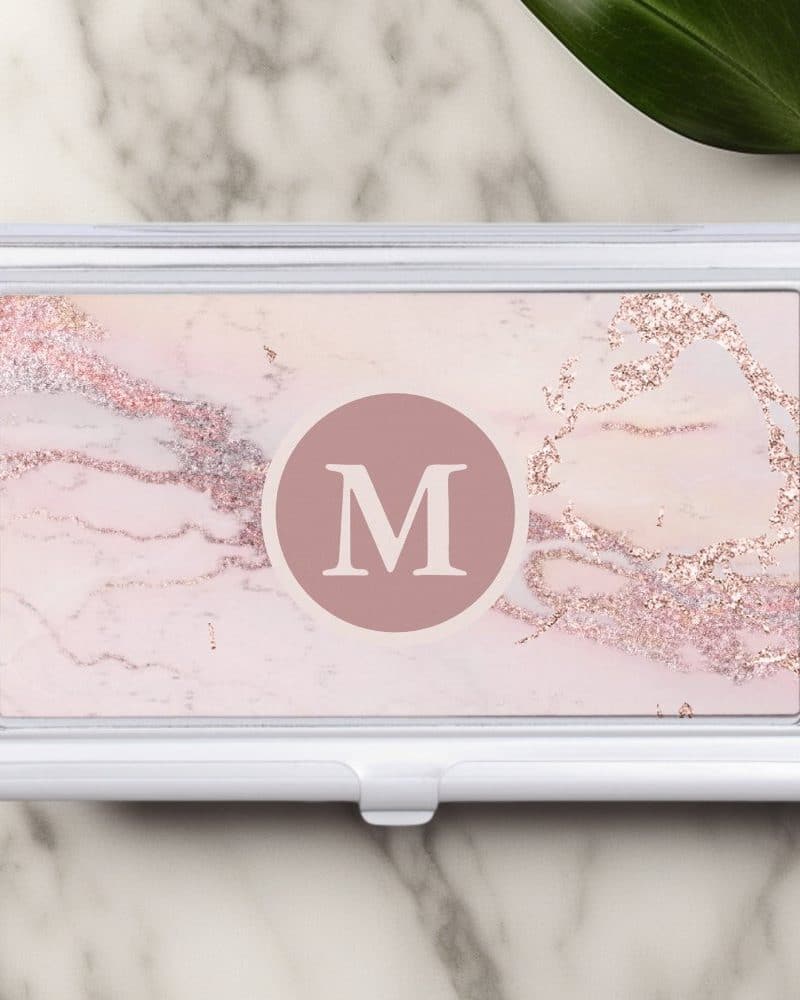 Silver business card holder with a pink marble design and a central letter M.