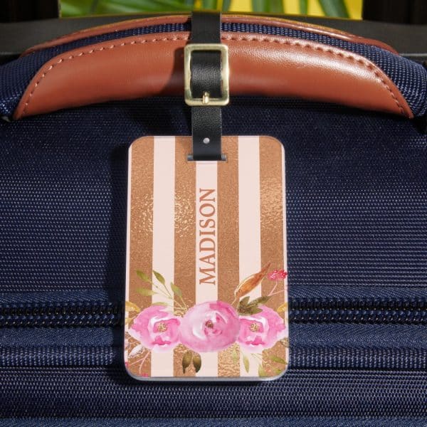 Pink Floral Luggage Tag With The Name Madison On A Pink And Gold Striped Background Attached To A Dark Blue Suitcase.