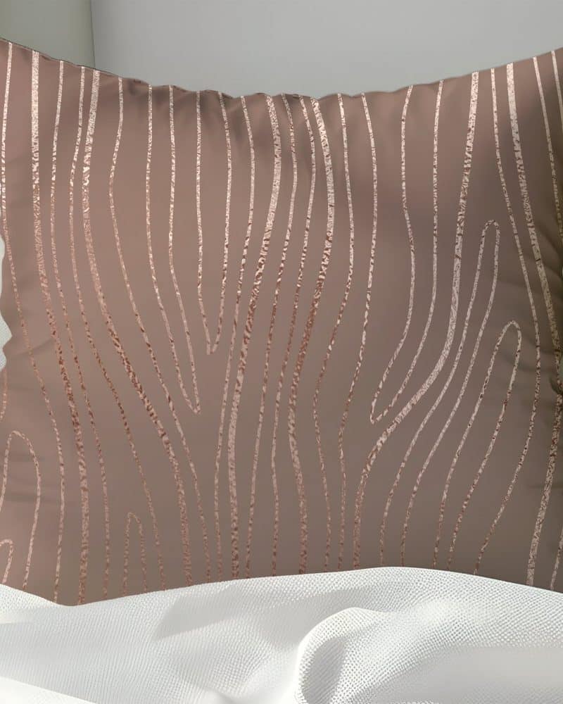Rose gold patterned throw pillow on a white bed.
