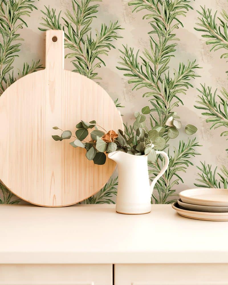 Large round wooden board and white pitcher with eucalyptus sprigs, set against a rosemary patterned wall.
