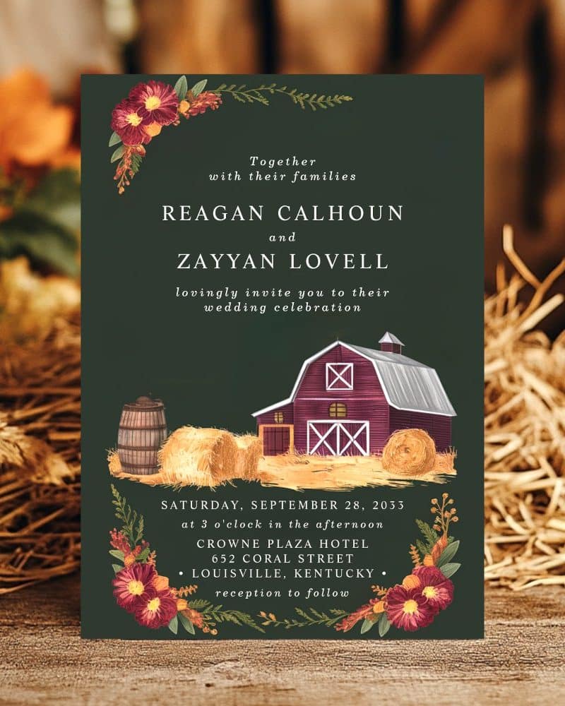 A dark green wedding invitation featuring a barn, hay bales, and autumnal floral accents.