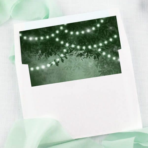 White Envelope With A Dark Green Insert Showing String Lights Among Tree Branches.