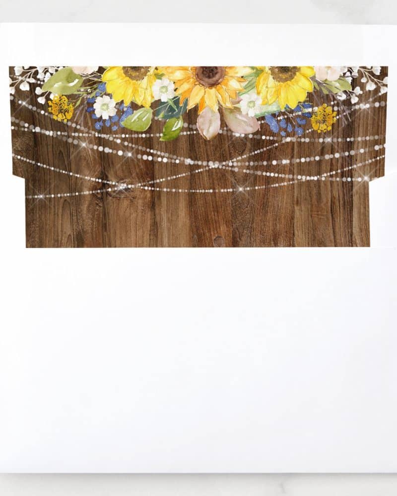 White envelope with a rustic wood background design featuring sunflowers, other flowers, and string lights.