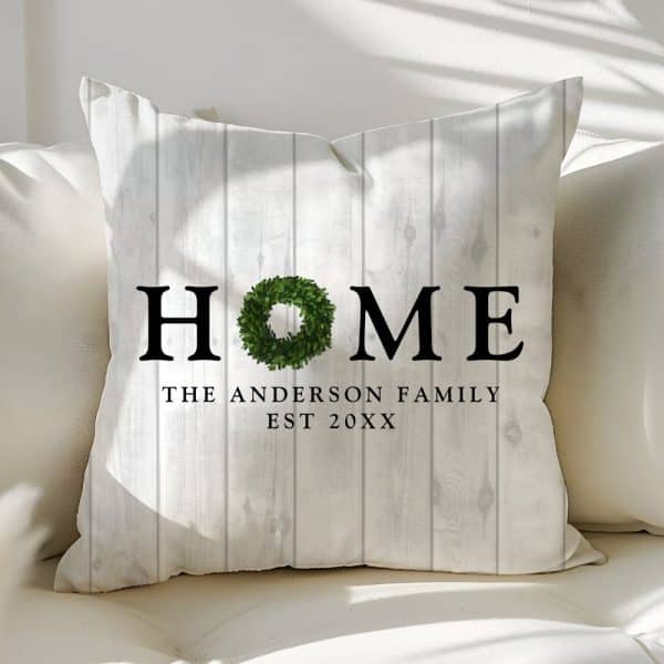 White Throw Pillow With The Word Home In Black Lettering, A Green Wreath Replacing The Letter O, And The Anderson Family Est 20Xx Below.