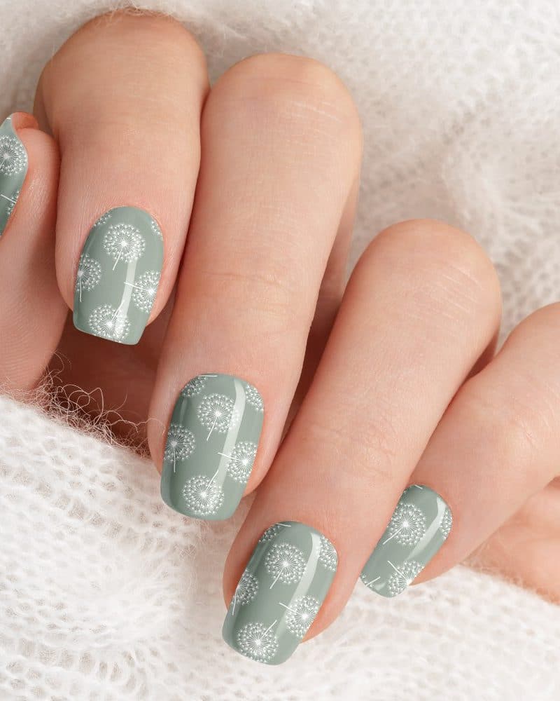 Close-up of a hand with pale green nails decorated with a white dandelion pattern.