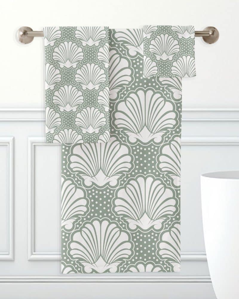 Sage green bath towels with a white seashell pattern hang on a rod.