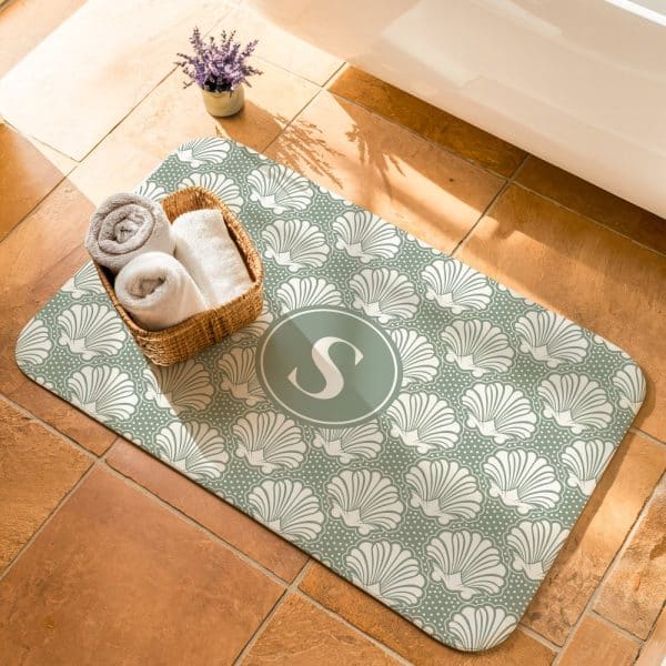 Sage Green Bath Mat With A Seashell Pattern And A Monogrammed S In The Center.