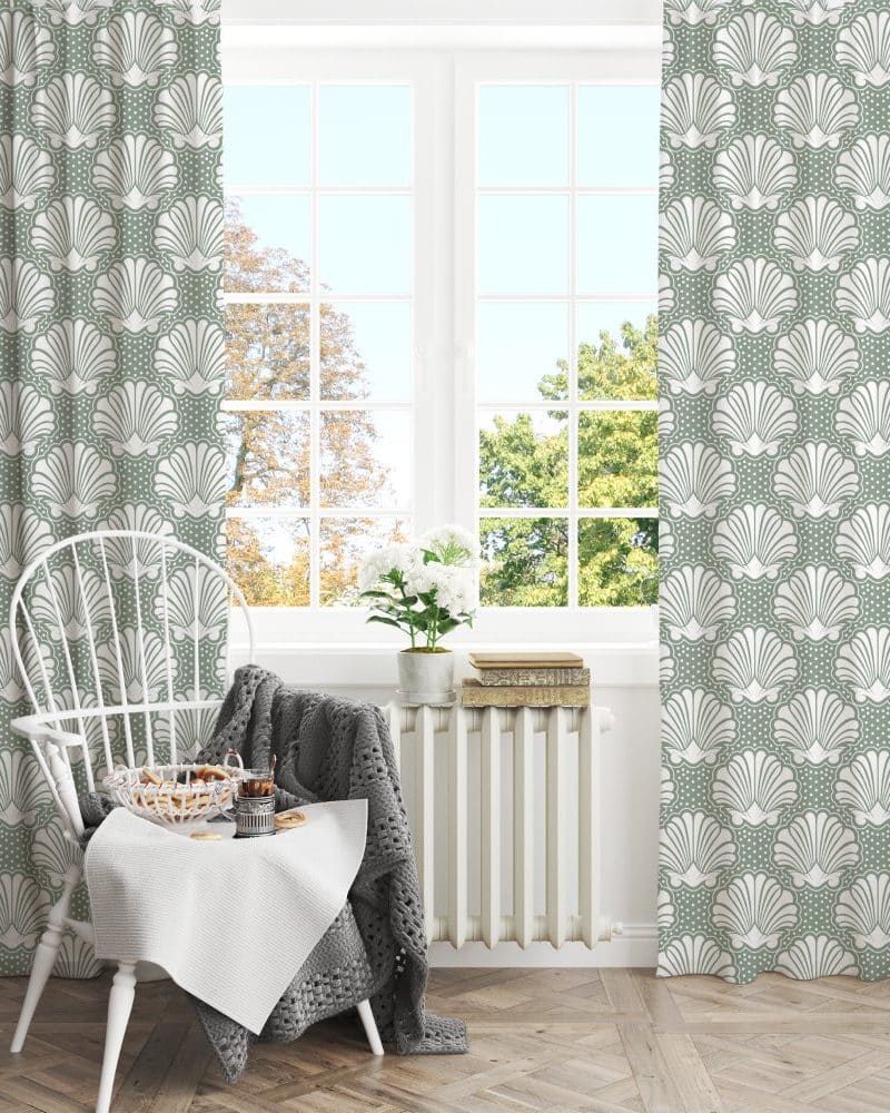 Sage green curtains with a white seashell pattern hang in a window, partially obscuring a view of a white chair and small table.