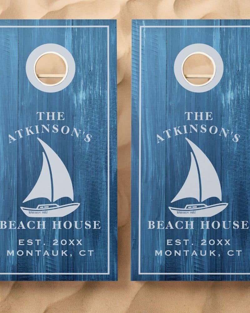 Pair of blue cornhole boards with the Atkinson's Beach House logo. Each board features a sailboat graphic.