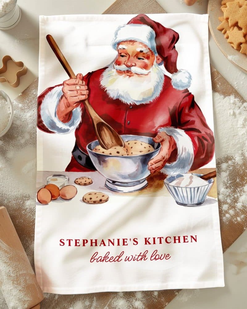 A kitchen tea towel featuring a vintage illustration of Santa Claus baking cookies.