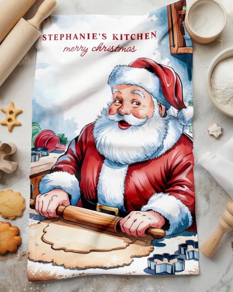 Kitchen tea towel featuring Santa Claus baking Christmas cookies.