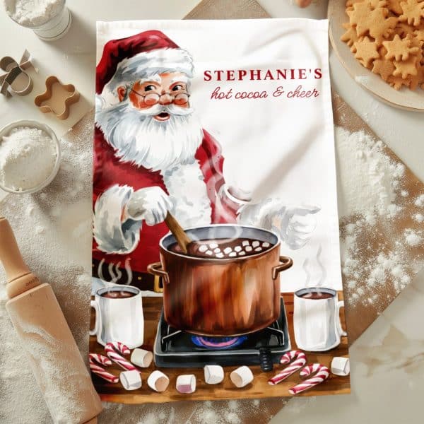 A Tea Towel Depicting Santa Claus Stirring A Pot Of Hot Cocoa On A Stovetop. The Towel Is Personalized With The Name Stephanie.
