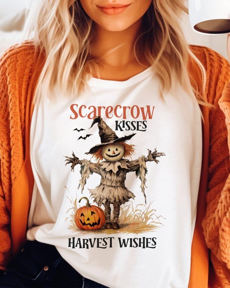 White shirt featuring a scarecrow design with a pumpkin and the text Scarecrow Kisses Harvest Wishes.