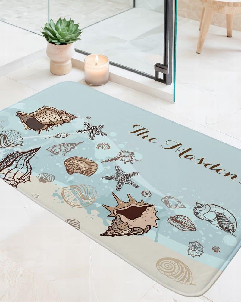 Light blue bath mat with a seashell and starfish design and the name "The Masdens".