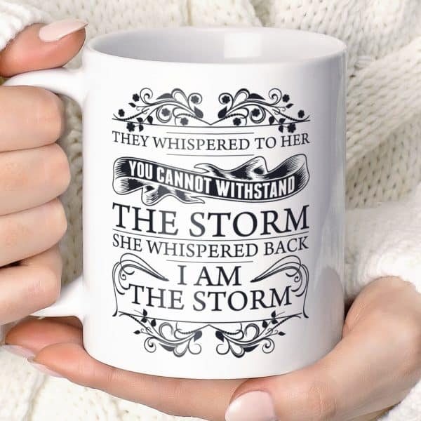 A White Coffee Mug With Black Text And Decorative Flourishes Reads, They Whispered To Her, You Cannot Withstand The Storm. She Whispered Back, I Am The Storm.