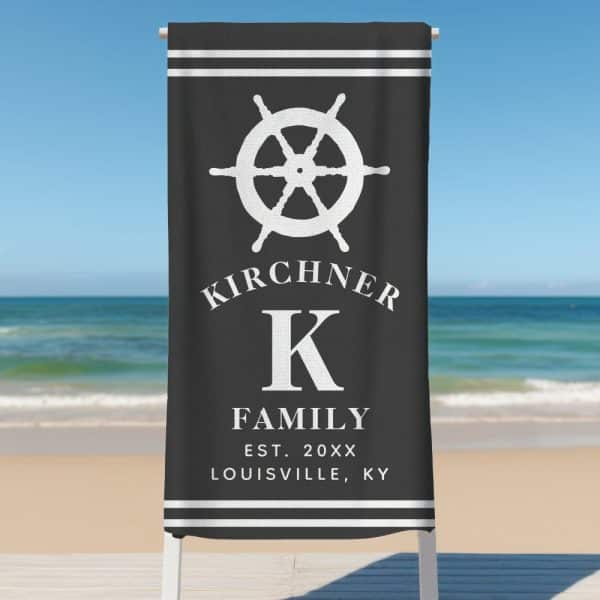 Black Beach Towel With A White Ship'S Wheel, The Letter K, And The Kirchner Family Name.
