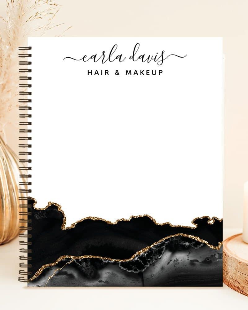 Spiral-bound notebook with Carla Davis Hair & Makeup logo, featuring a black and gold agate design.