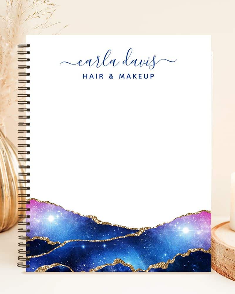 Spiral-bound notebook with Earla Davis Hair & Makeup logo; bottom features a galaxy design with gold accents.