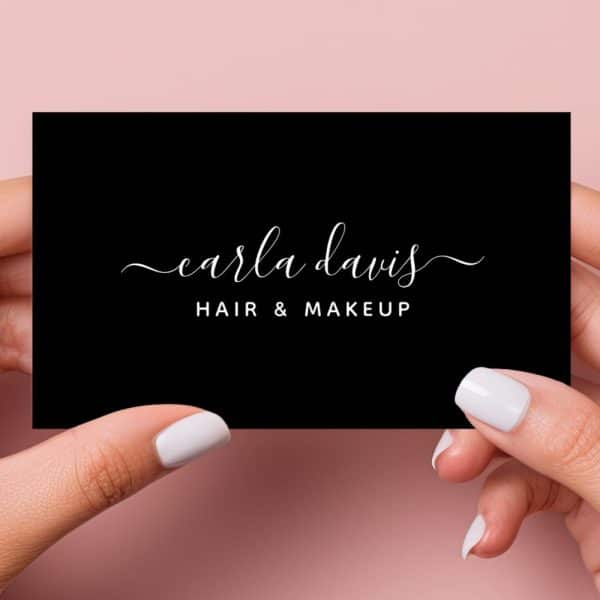 Two Hands Hold Up A Black Business Card With Carla Davis Hair &Amp; Makeup Written In Elegant White Script.