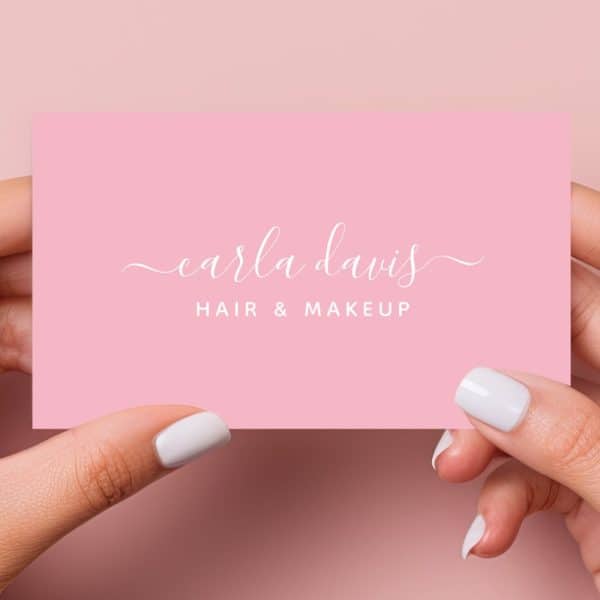 Two Hands Hold A Pink Business Card With Carla Davis Hair &Amp; Makeup In White Script.