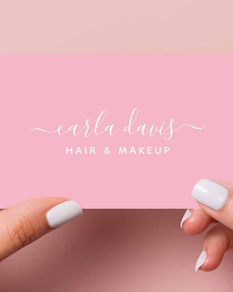Two hands hold a pink business card with Carla Davis Hair & Makeup in white script.