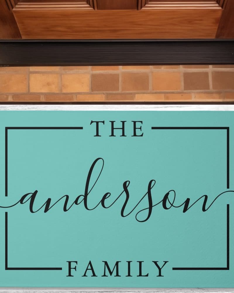 Teal welcome mat with the text The Anderson Family in a black sans-serif font.