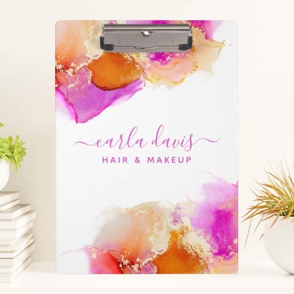 A Clipboard With An Abstract Watercolor Design In Pink, Orange, And Gold, Featuring The Name Carla Davis Hair &Amp; Makeup.