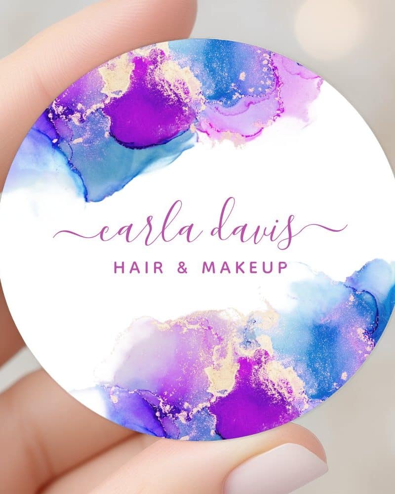 Round business card featuring purple and blue watercolor design with gold accents, displaying Carla Davis Hair & Makeup.