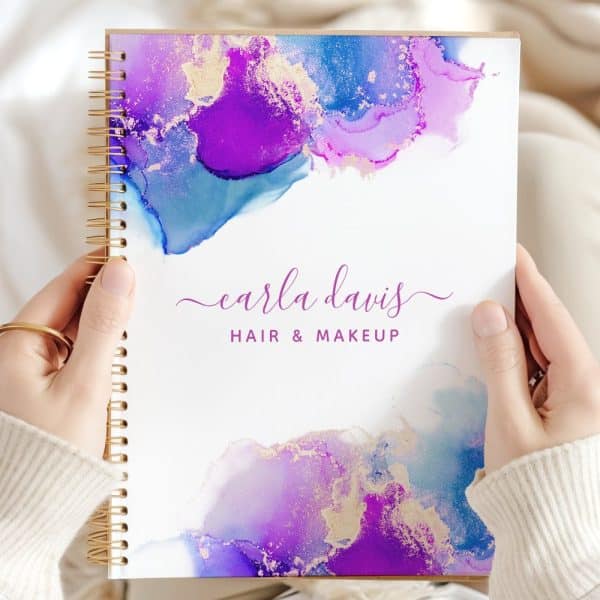 Two Hands Hold A Spiral-Bound Notebook Featuring An Abstract Purple, Blue, And Gold Design And The Text Carla Davis Hair &Amp; Makeup.