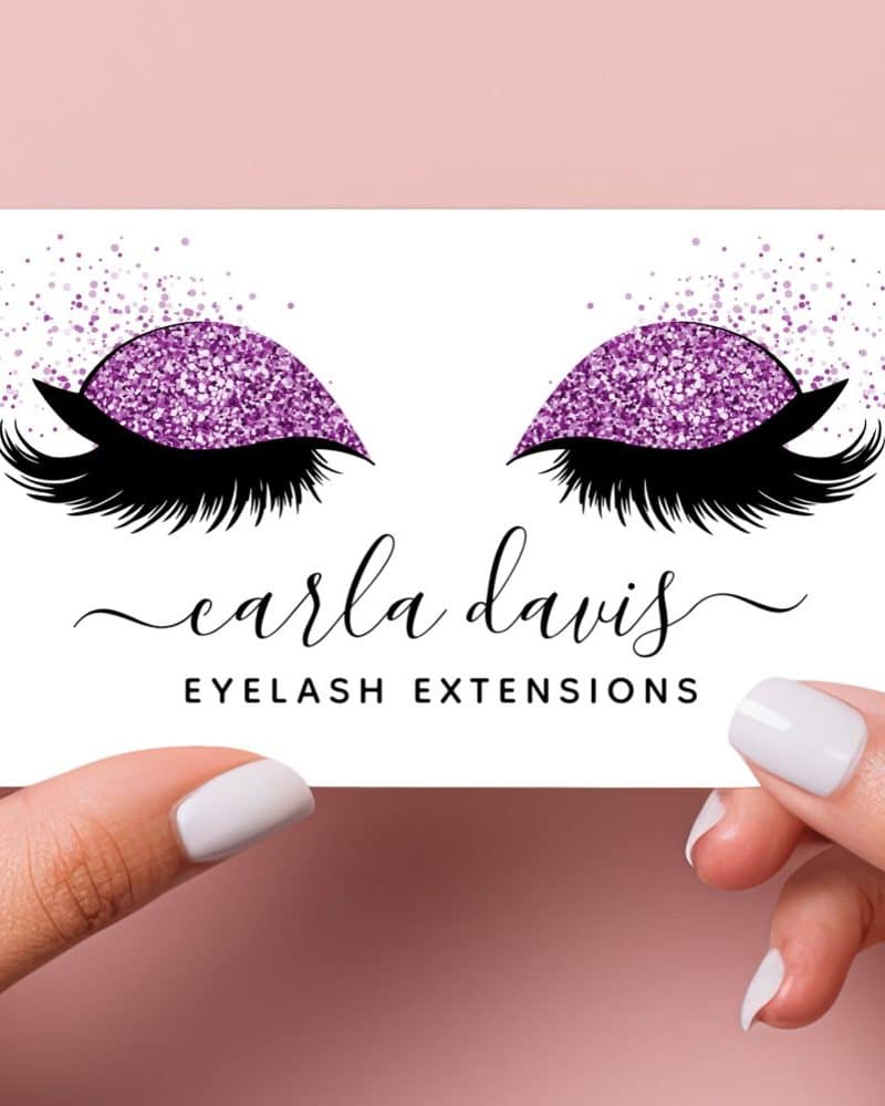 Business card featuring a pair of eyes with purple glitter eyeshadow and long lashes; Carla Davis Eyelash Extensions.
