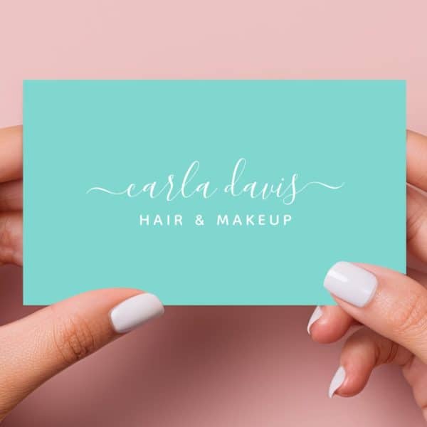 Two Hands Hold Up A Teal Business Card With Carla Davis Hair &Amp; Makeup Written In A Script Font.