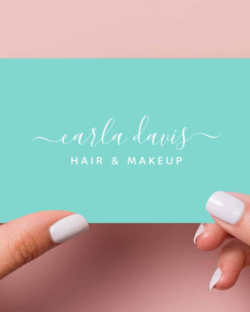 Two hands hold up a teal business card with Carla Davis Hair & Makeup written in a script font.