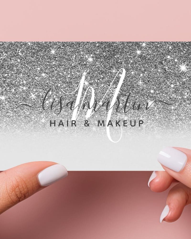 Two hands hold a silver glitter business card for Lisa Martin Hair & Makeup.