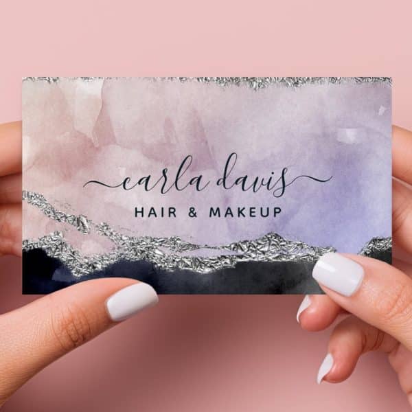 Two Hands Hold A Business Card Featuring A Watercolor Design In Shades Of Purple And Pink, Accented With Silver Foil. The Name Carla Davis, Hair &Amp; Makeup Is Displayed In Elegant Script.