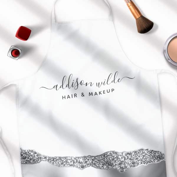 White Apron With The Name Addison Wilde, Hair &Amp; Makeup, And A Silver Glitter Design At The Bottom.