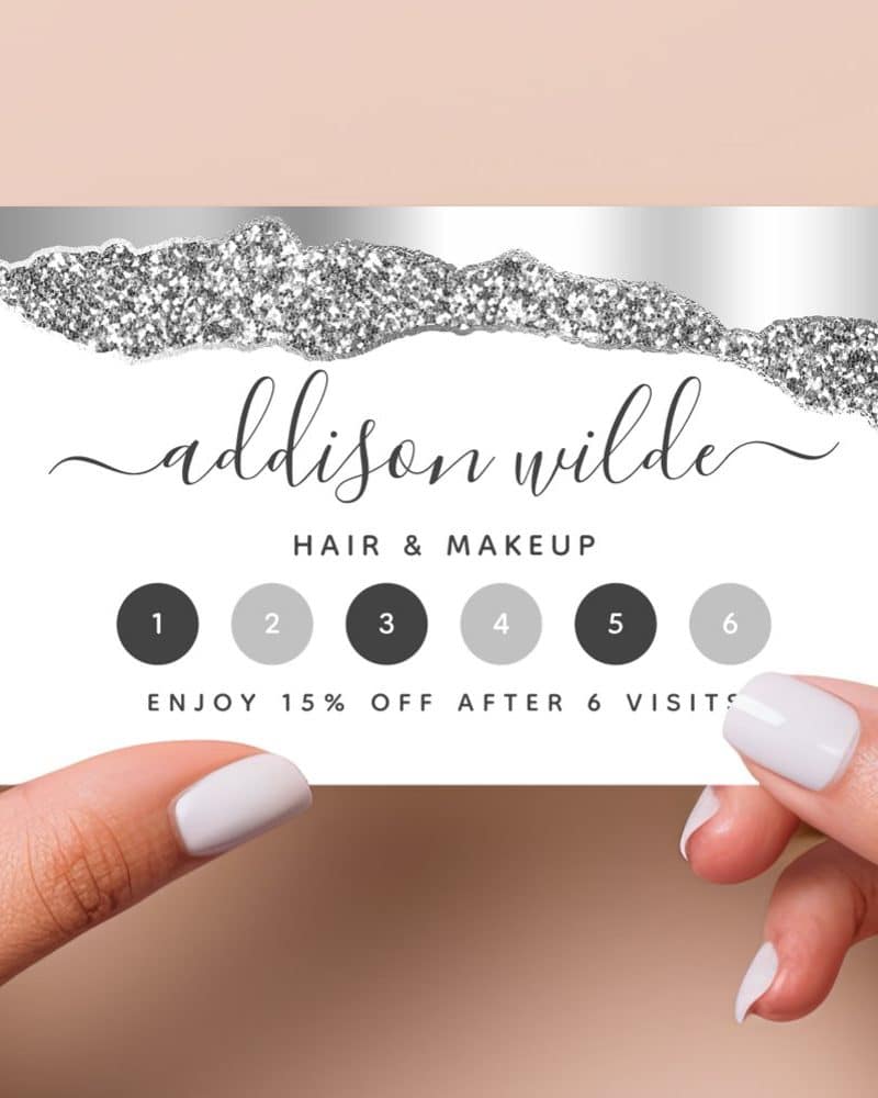 A silver and white loyalty card for Addison Wilde Hair & Makeup. The card has a glitter design and six spaces to be punched for visits, offering a 15% discount after six visits.