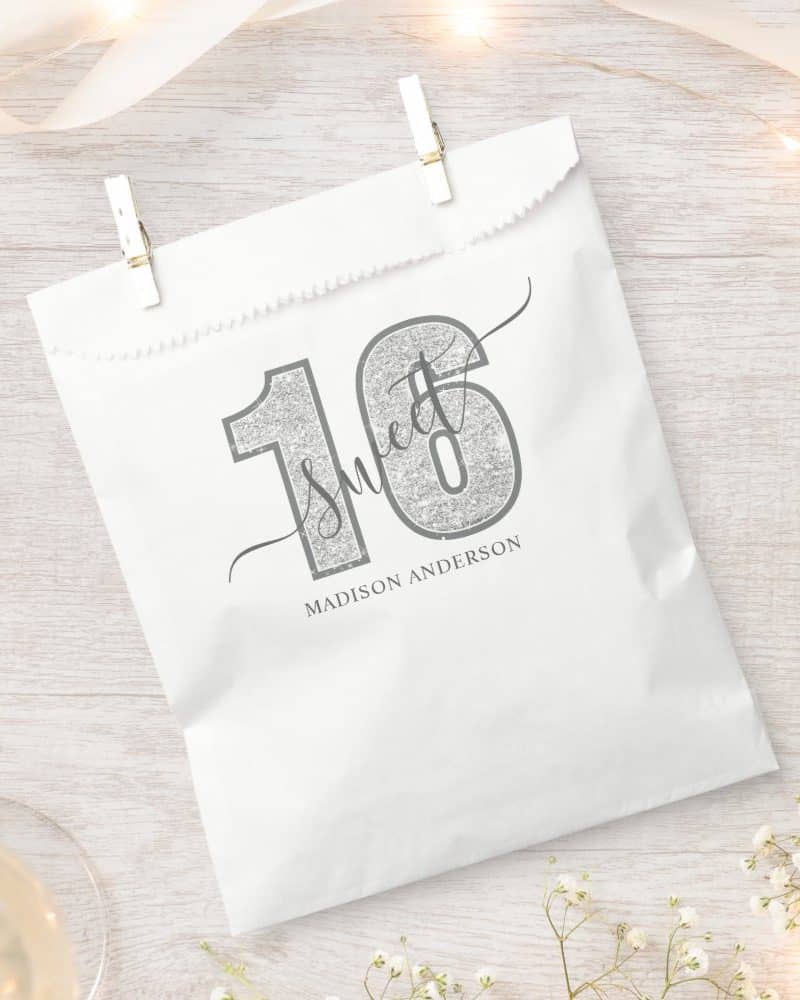 Silver glitter-textured number sixteen with the word sweet and Madison Anderson's name printed on a white gift bag.