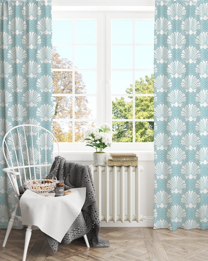 Light blue curtains with a white seashell pattern hang in front of a window.