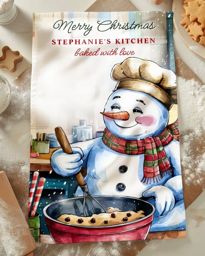 Christmas tea towel featuring a snowman chef baking in a kitchen.