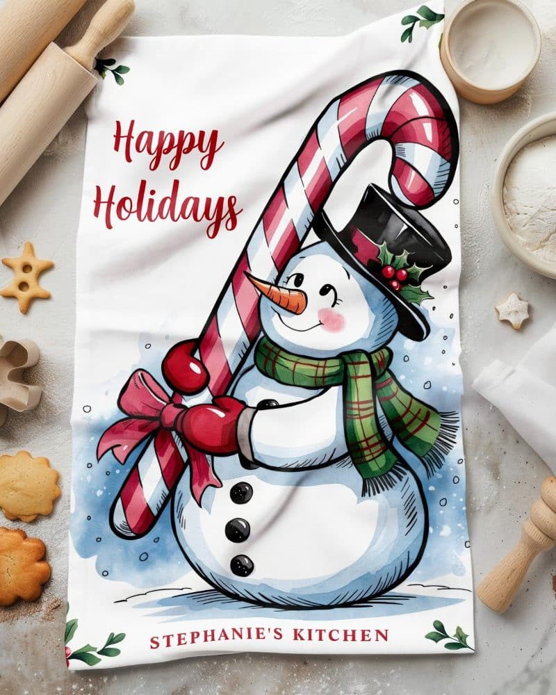 Kitchen towel with a happy holidays message and illustration of a snowman holding a candy cane.