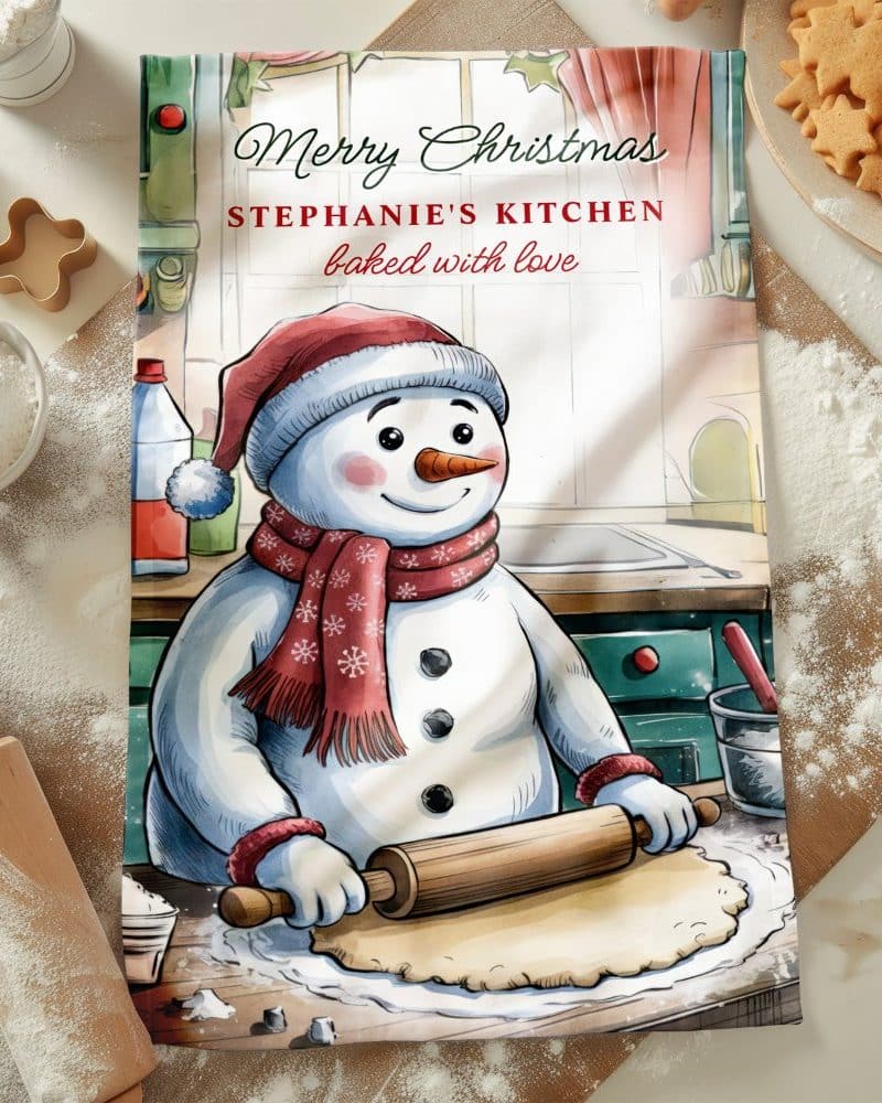 A Christmas-themed kitchen towel featuring a snowman baking.