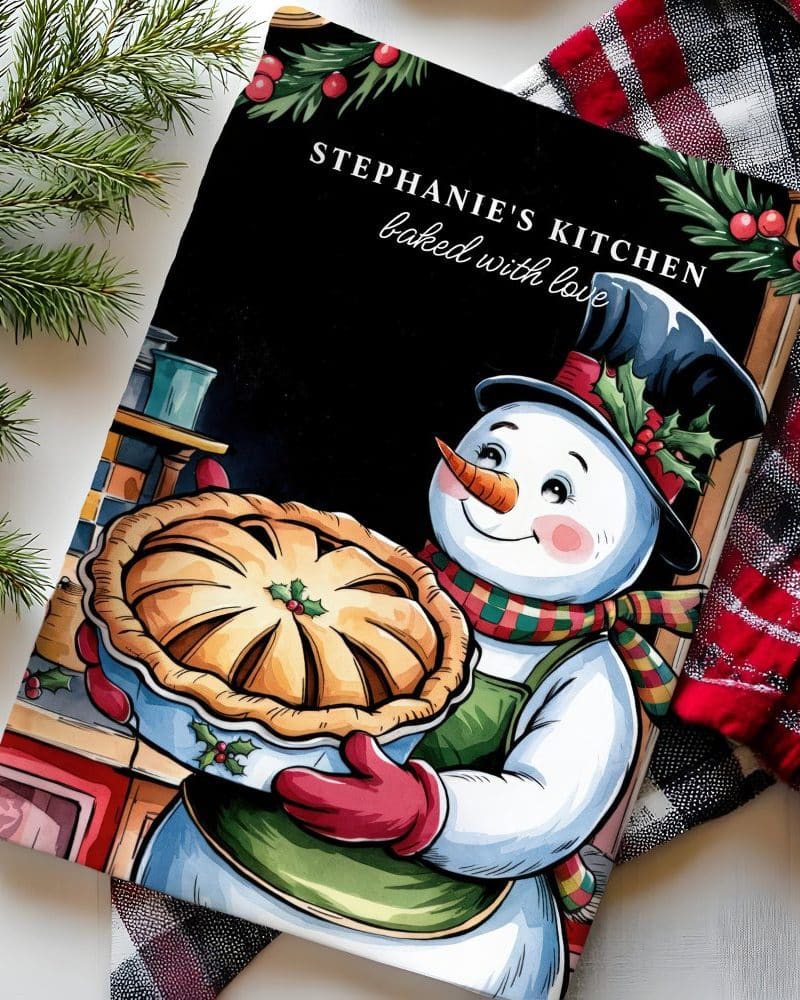 A snowman holding a pie, on a cookbook cover titled Stephanies Kitchen, baked with love.
